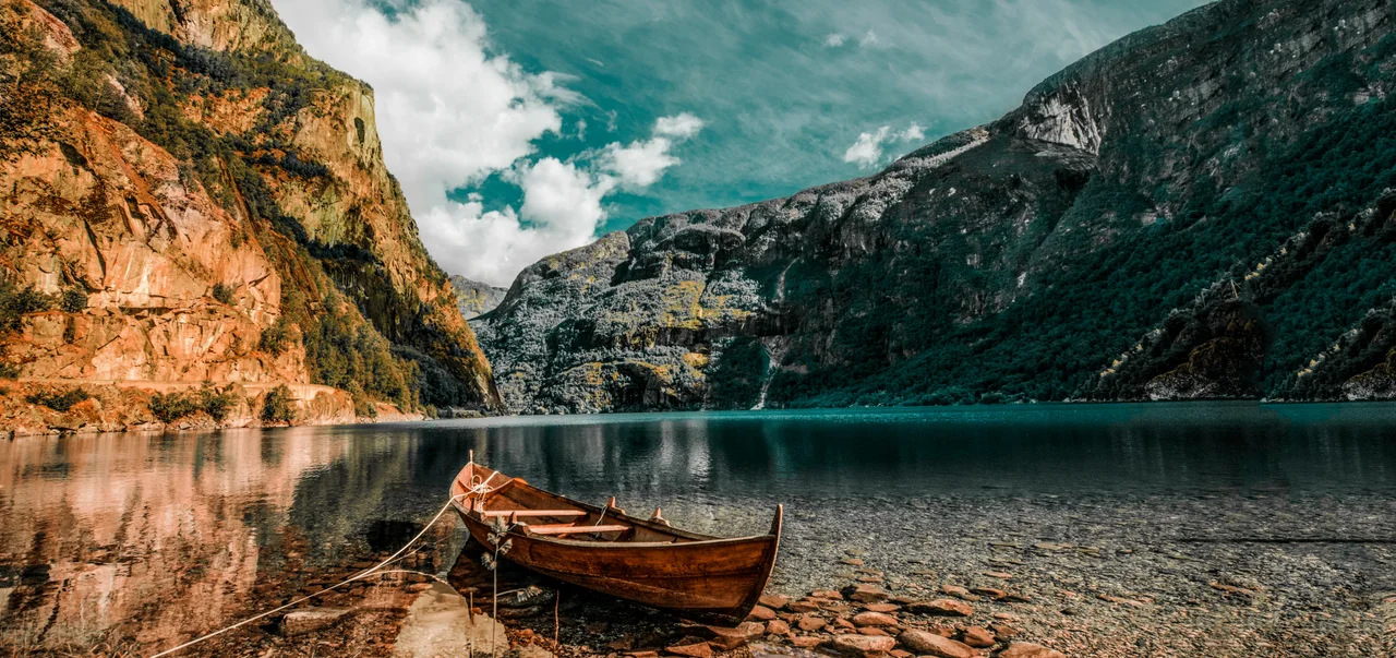A wooden boat on a clear mountain lake, beneath autumn cliffs.